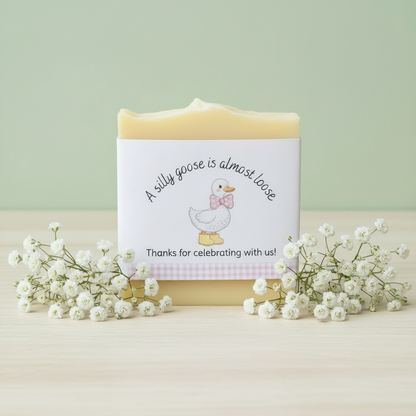 Bar of soap with a decorative label featuring a silly goose illustration on a light surface with flowers. 